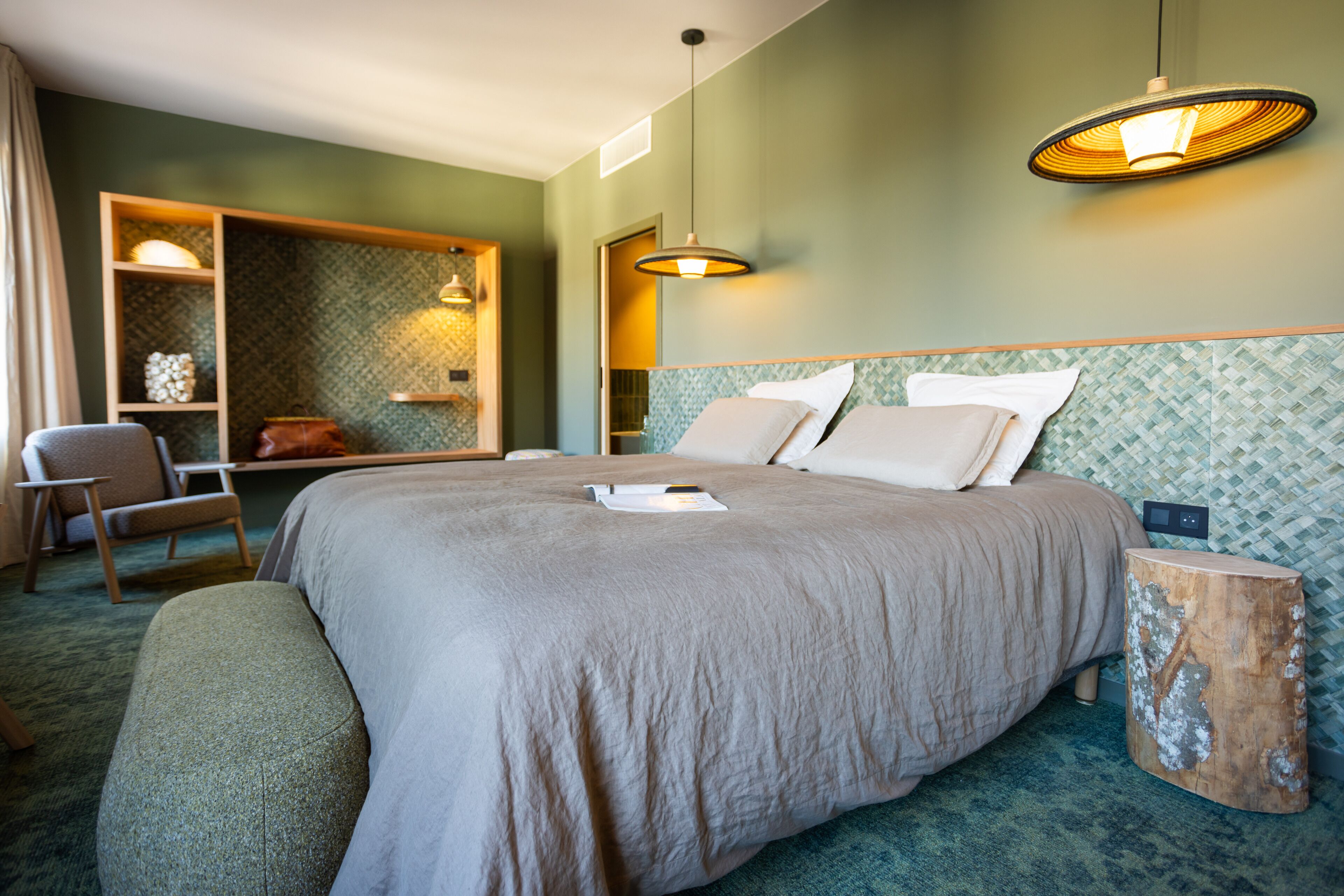Habitación de hotel ordenada con una cama grande, una silla, una mesita auxiliar y un taburete de madera original.