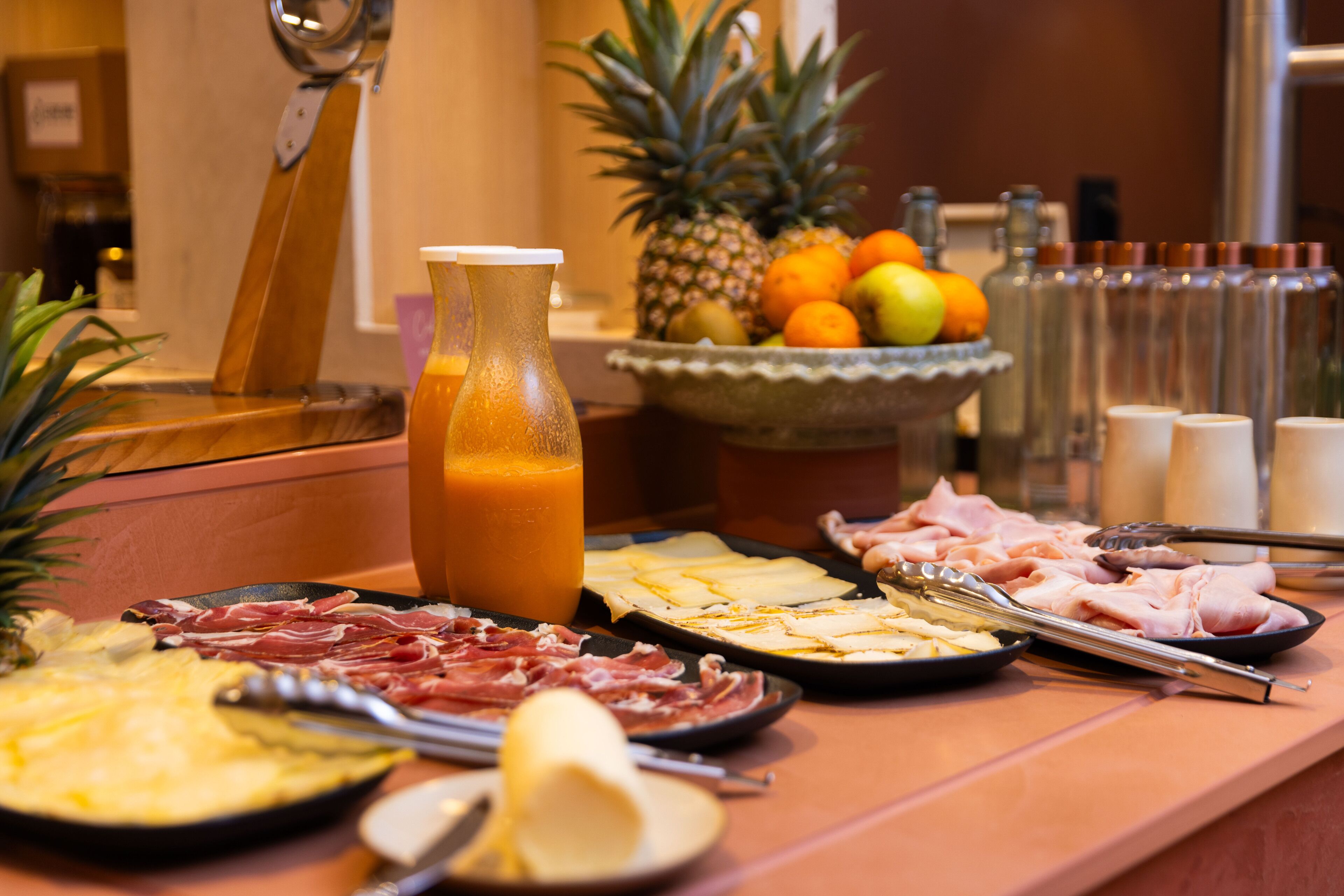 A breakfast buffet with various meats, cheeses, fruits, and a juice pitcher.