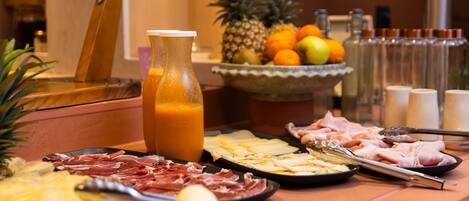 A breakfast buffet with various meats, cheeses, fruits, and a juice pitcher.