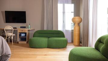 A modern living room with a green sofa, a wooden desk with a flat-screen TV, a wicker chair, and a tall woven lamp.