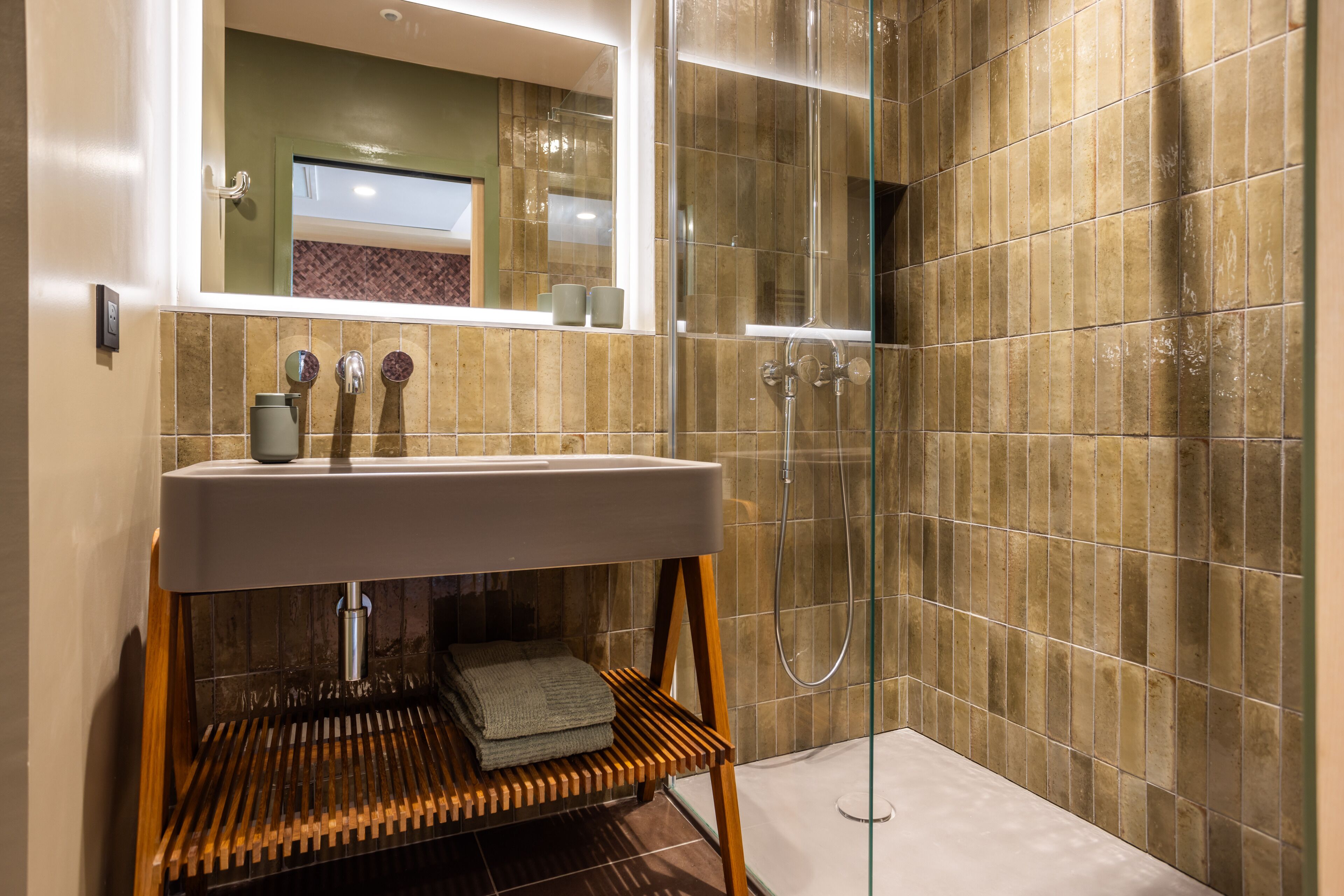 Um banheiro moderno com toucador de madeira, box de vidro e parede revestida em azulejos.