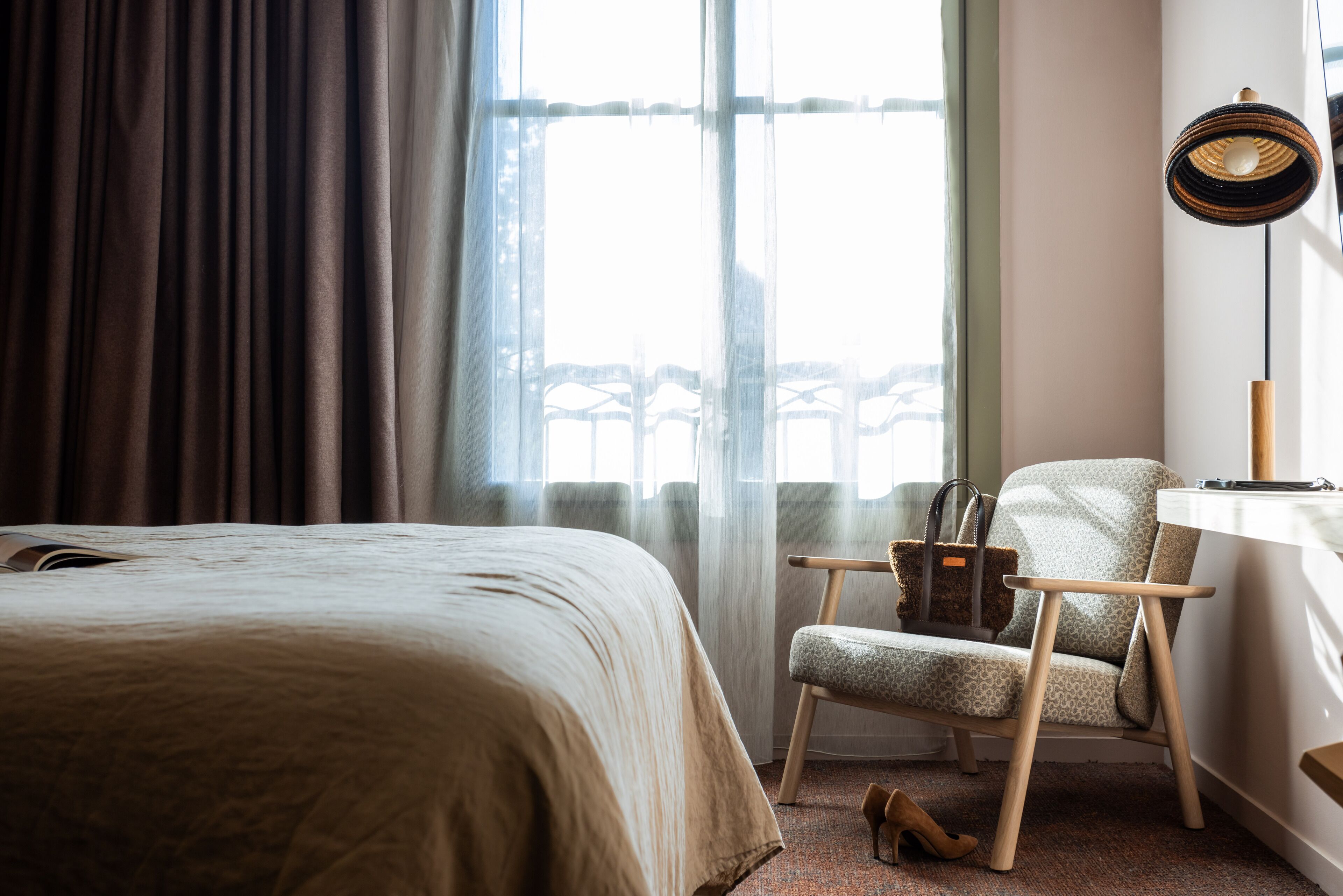 A hotel room with a bed, a chair, a lamp, and a view of the outside.
