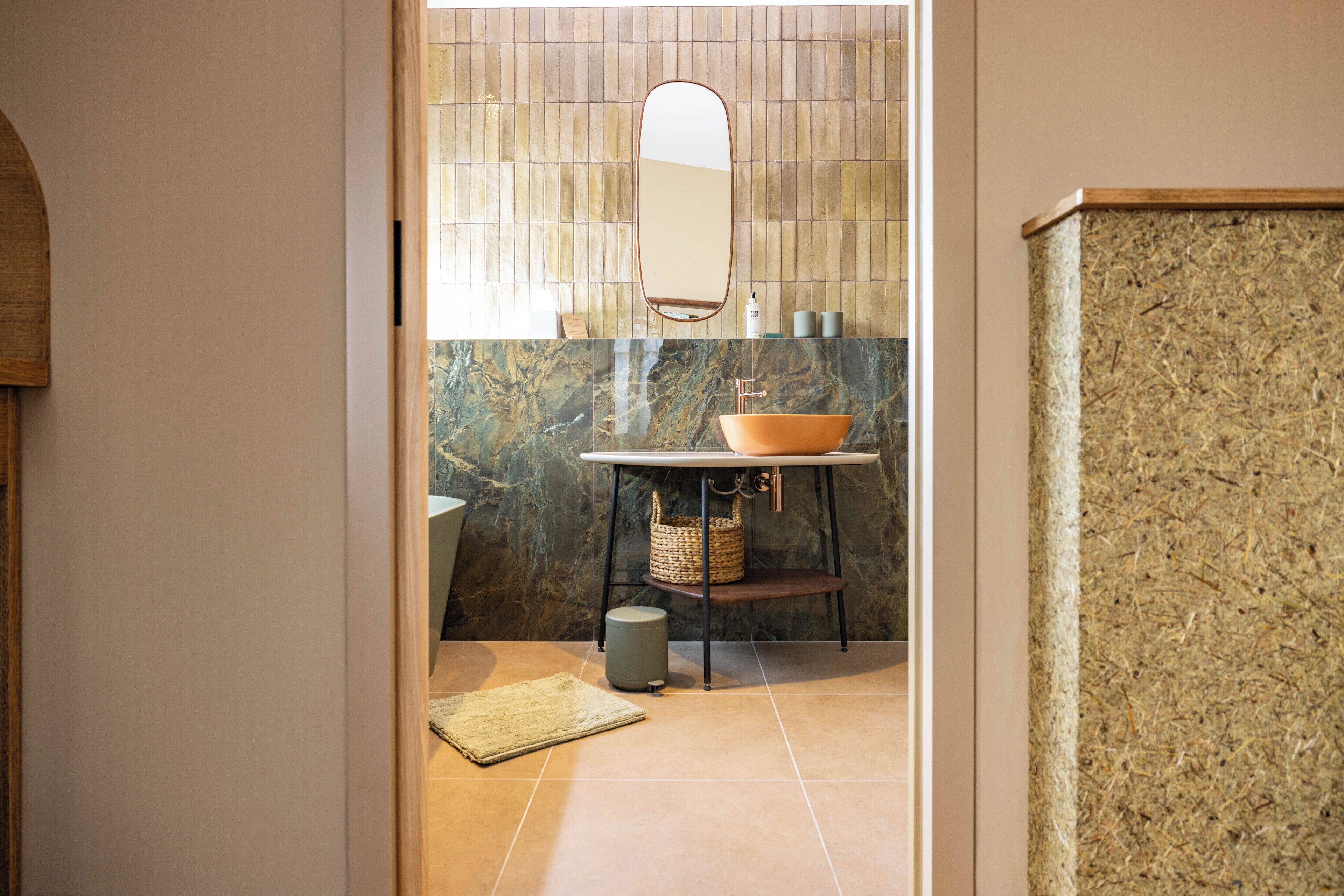 Une salle de bain avec un lavabo en marbre, un miroir rond et un mur à texture.