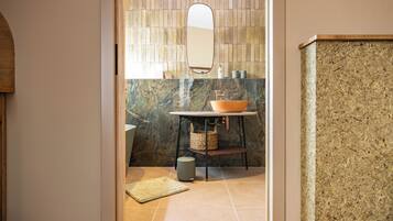 Une salle de bain avec un lavabo en marbre, un miroir rond et un mur à texture.