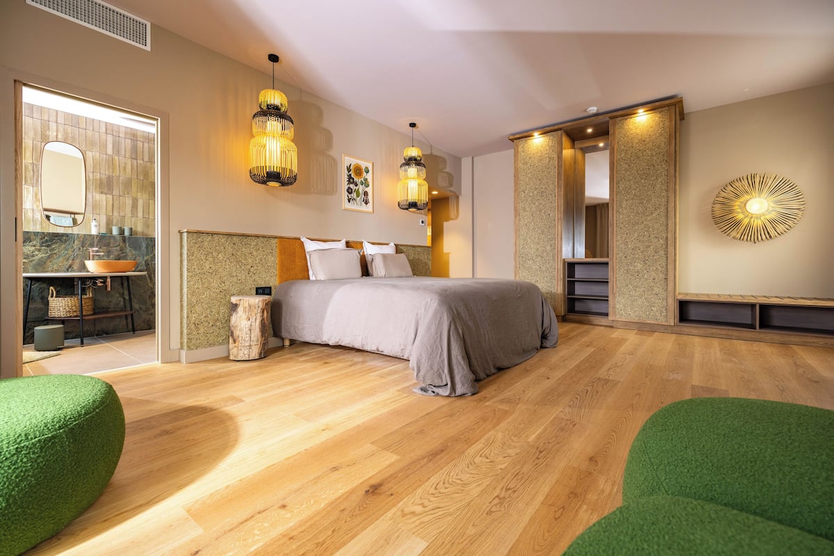 Une chambre moderne avec un grand lit, un plancher en bois et un banc recouvert d’un tissu vert.
