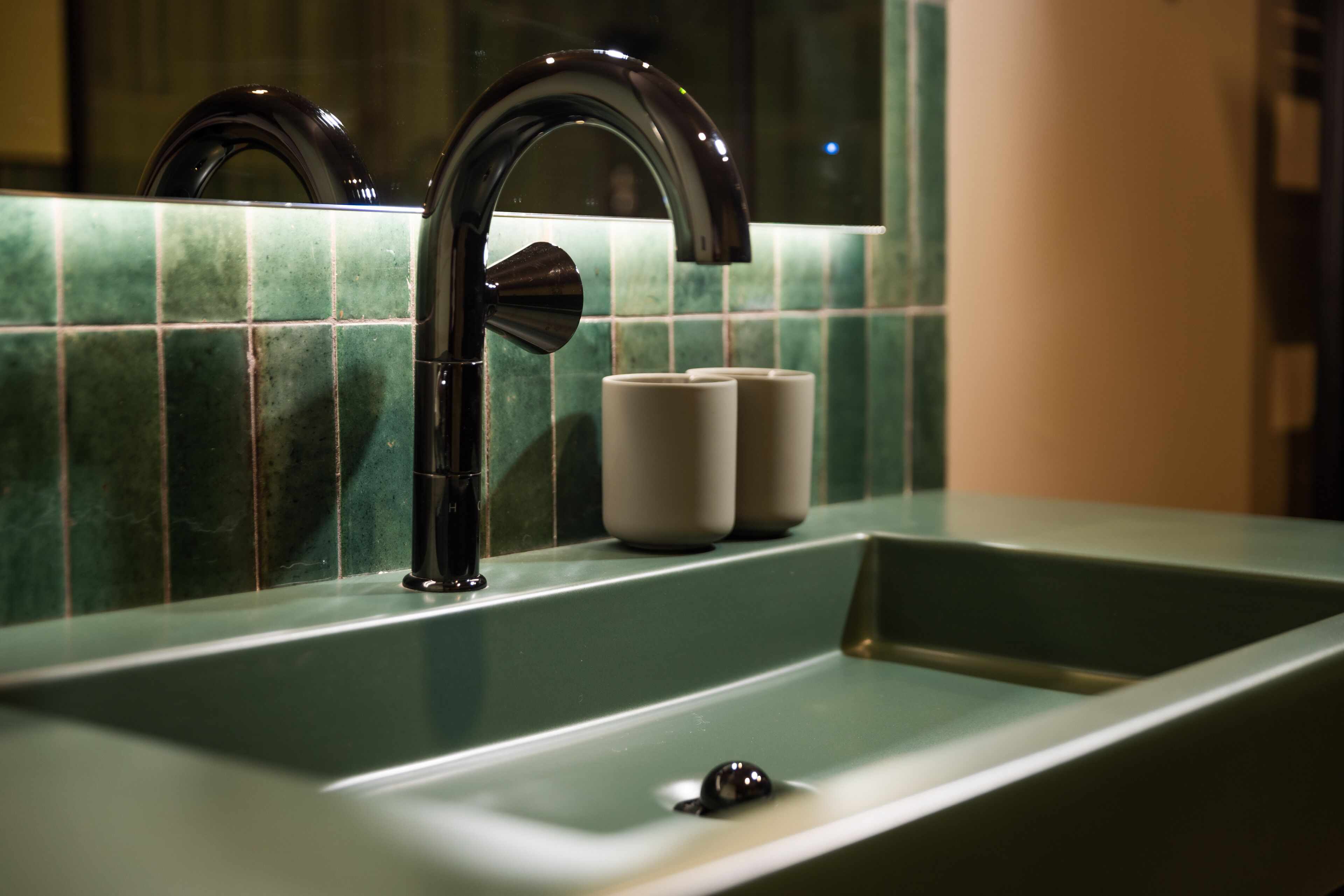 Un lavamanos de baño con una llave moderna y azulejos verdes.
