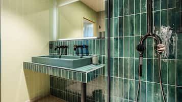 A bathroom with a rectangular sink, two faucets, and a showerhead.