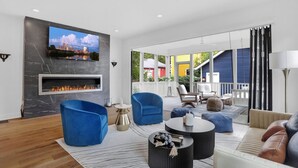 Een moderne woonkamer met een open haard, blauwe fauteuils en een grote tv die aan de muur is bevestigd.