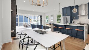 Een moderne keuken met donkerblauwe kastjes, een wit kookeiland met barkrukken, en een grote eettafel.