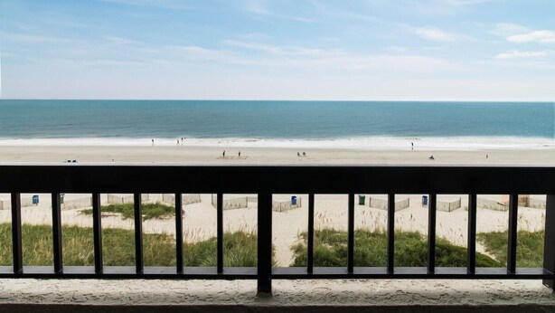 Blick auf einen Strand vom Balkon mit Geländer, feinem Sand und dem Meer.