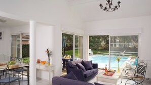 Un salon moderne avec vue sur la piscine, des meubles blancs et un coin repas avec une table dressée pour deux personnes.