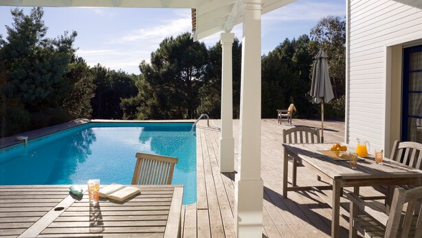 Une terrasse en bois avec une piscine, du mobilier d’extérieur et une pergola.