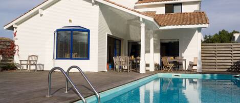 Ein Haus mit Schwimmbad, einer Terrasse mit Stühlen und einem überdachten Außenbereich.