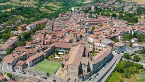 Une vue aérienne d’une ville historique, avec une place centrale bordée de bâtiments aux toits recouverts de tuiles rouges, et une église imposante surmontée d’un dôme.