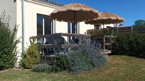 Een terras met twee rieten parasols, een houten dek en diverse planten.