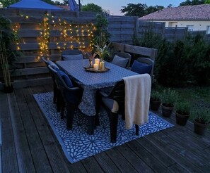 Eine Terrassenausstattung im Freien mit einem Tisch für vier Personen, umgeben von Stühlen, einem gemusterten Teppich und Topfpflanzen.