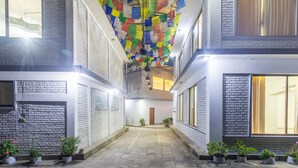 A courtyard with brick walls, potted plants, and colorful flags hanging from the ceiling.