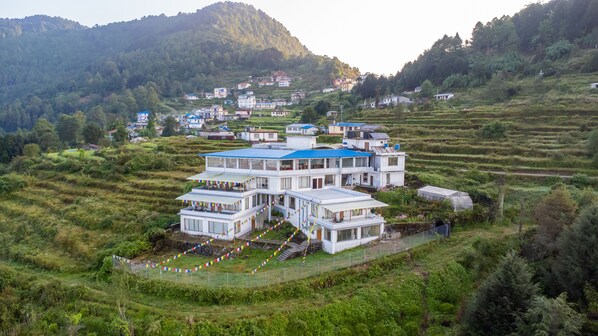 A multi-story building with a flat roof, surrounded by terraced fields and a mountainous backdrop.