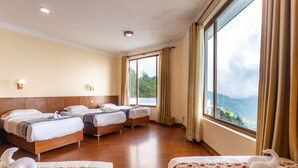 A hotel room with three beds, a large window with curtains, and a view of a mountainous landscape.