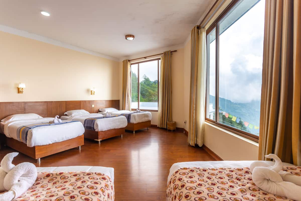 Habitación de hotel con tres camas, un ventanal con cortinas y vista a un paisaje montañoso.