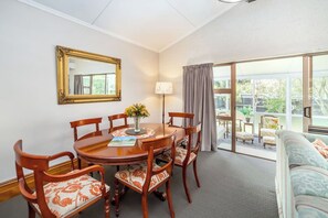 A dining area with a round table, six chairs, a vase of flowers, and a framed mirror on the wall. - The Farmhouse On Church (Greytown)