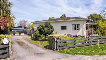 A single-story house with a paved driveway, a wooden fence, and a variety of shrubs and small trees.