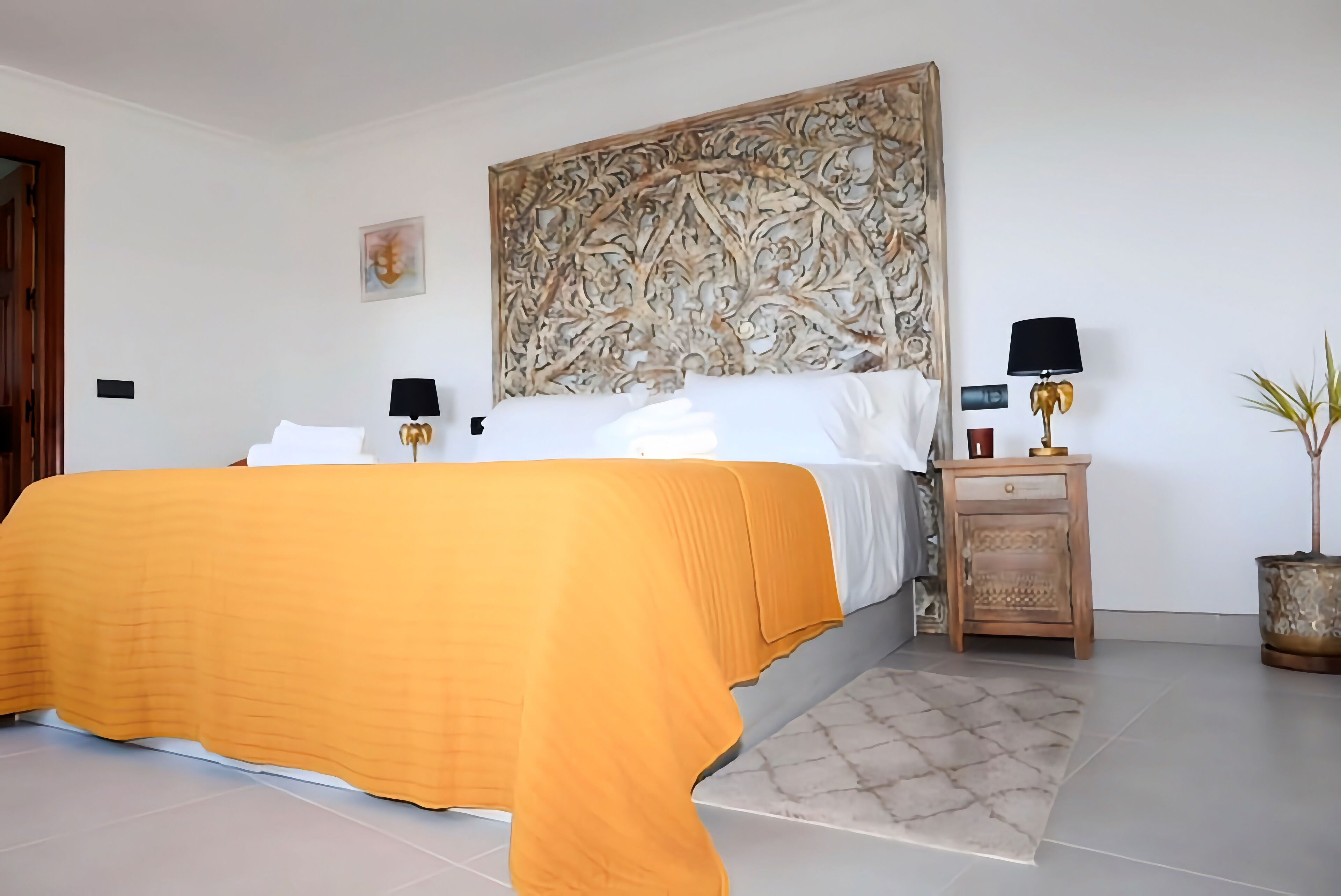 Un dormitorio con cama, mesita de noche, lámpara y un cabecero decorativo.