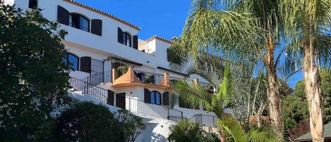 A white building with balconies and a pool area with lounge chairs.