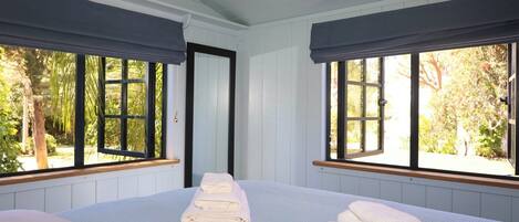 A room with two beds, large windows with dark curtains, and a view of greenery outside.