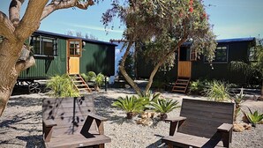 A campsite with wooden benches, a tree, and green buildings with windows and doors. - La Piña Verde (Estepona)