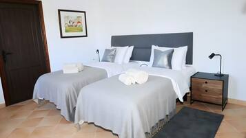 A hotel room with two beds, a nightstand, a desk, a chair, a door, and a framed picture on the wall.