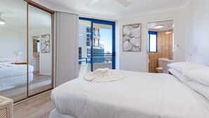 Une chambre d’hôtel moderne avec un grand lit, un balcon doté de balustrades bleues et une vue sur un immeuble situé de l’autre côté de la rue.