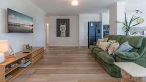 Un salon moderne avec un canapé vert, une table d’appoint en bois et un téléviseur à écran plat fixé au mur.