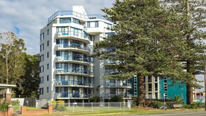 Un immeuble à plusieurs étages doté de balcons, entouré d’arbres et d’une clôture blanche.