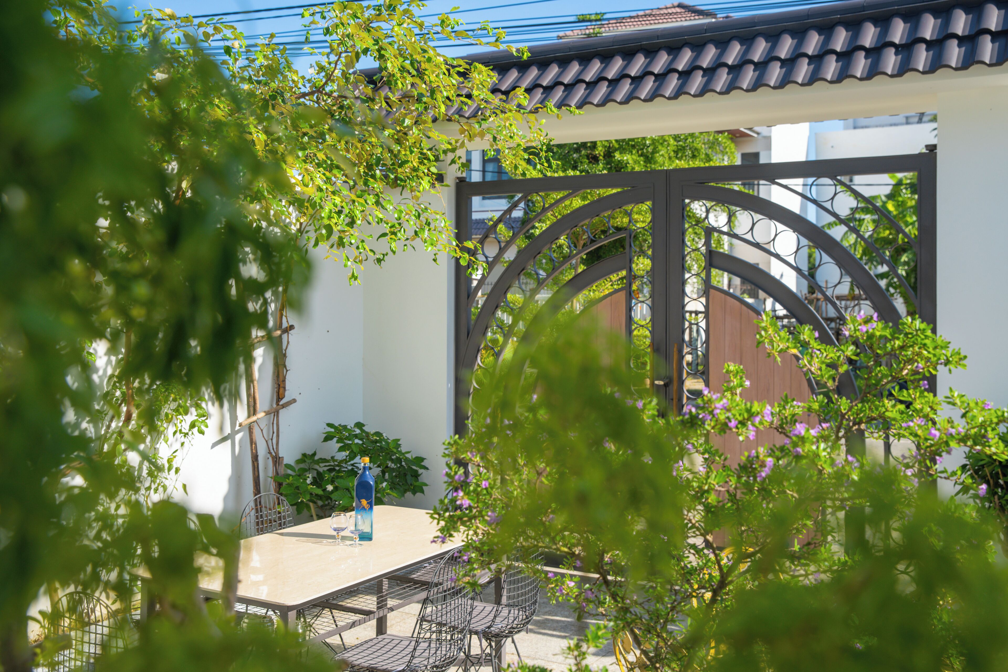 Eine Terrasse mit Tisch und Stühlen, umgeben von Grünpflanzen und einem dekorativen Metallzaun.
