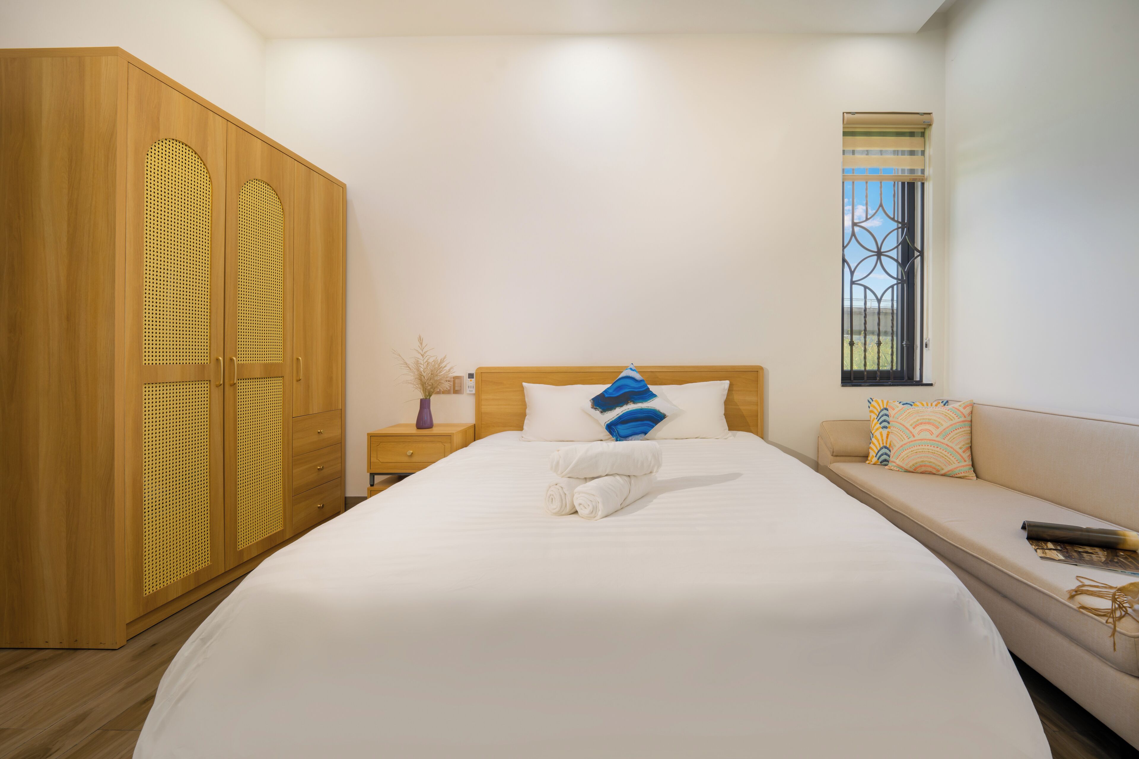 A hotel room with a large bed, wooden wardrobe, and a small sofa.