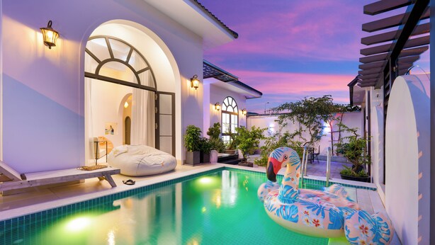 Una piscina con una silla de flamenco flotante, un sillón inflable blanco y una planta en maceta.