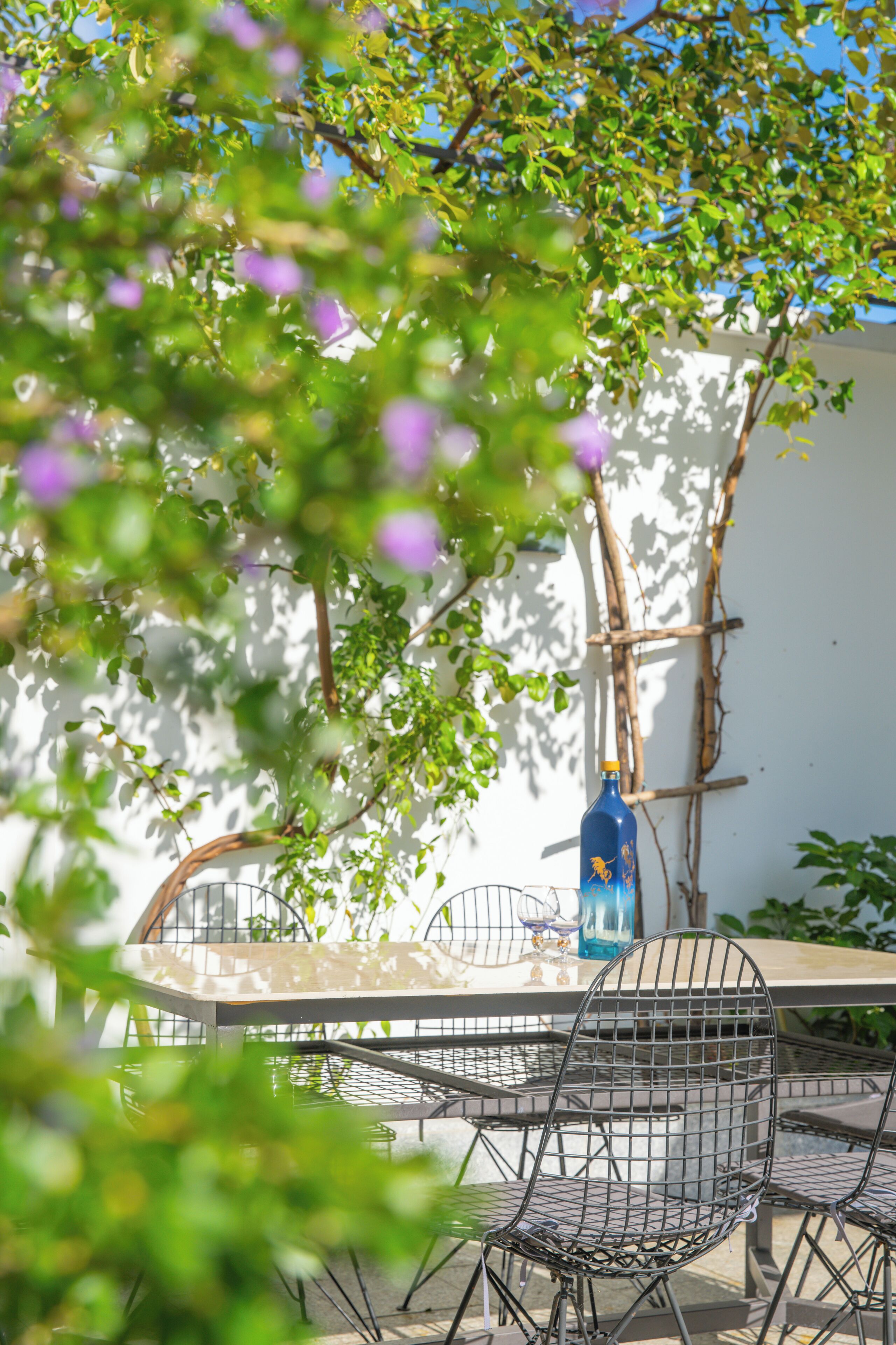 A patio with a metal table and chairs, a blue bottle, and a wall with climbing plants.