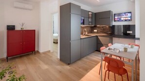 Une cuisine moderne avec des meubles gris, un meuble rouge et un coin repas avec des chaises orange.