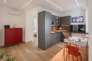 Una cocina moderna con armarios grises, un armario rojo, una mesa de comedor con sillas y un televisor montado sobre la encimera.