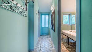A narrow hallway with patterned floor tiles, a blue door, and a bed with a patterned bedspread in a room with a window. - 1 bedroom gorgeous apartment in Gondolici (Gondolici)