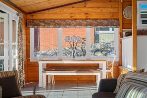 A wooden interior with a bench, a dining table, and a window with a view of a brick wall and trees. - Highfield Ride - Spa Pool, Ride the Redwoods (Rotorua)