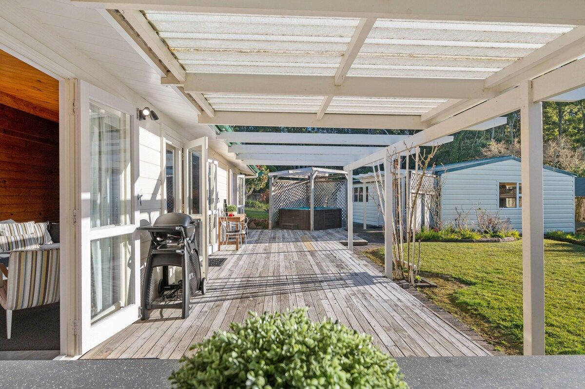 A covered outdoor deck with a grill and seating area, leading to a house with a fenced yard.