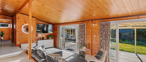 A modern log cabin interior with a living area, sofa, TV, and sliding glass doors leading to a deck.