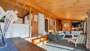 A wooden interior with a sofa, a TV, and a staircase leading to a kitchen. - Highfield Ride - Spa Pool, Ride the Redwoods (Rotorua)
