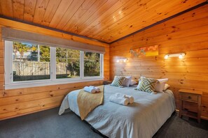 A wooden-paneled bedroom with a large window, a bed with pillows, and a bedside table. - Highfield Ride - Spa Pool, Ride the Redwoods (Rotorua)