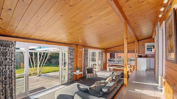 A spacious living area with a sofa, a dining table, and a kitchen in the background. - Highfield Ride - Spa Pool, Ride the Redwoods (Rotorua)