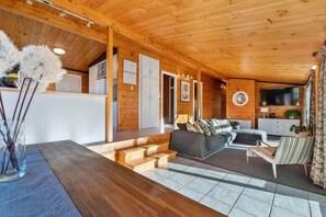 Ein Holzinnenraum mit einer Couch, einem an der Wand montierten Fernseher und einer Treppe, die zu einer oberen Ebene führt.