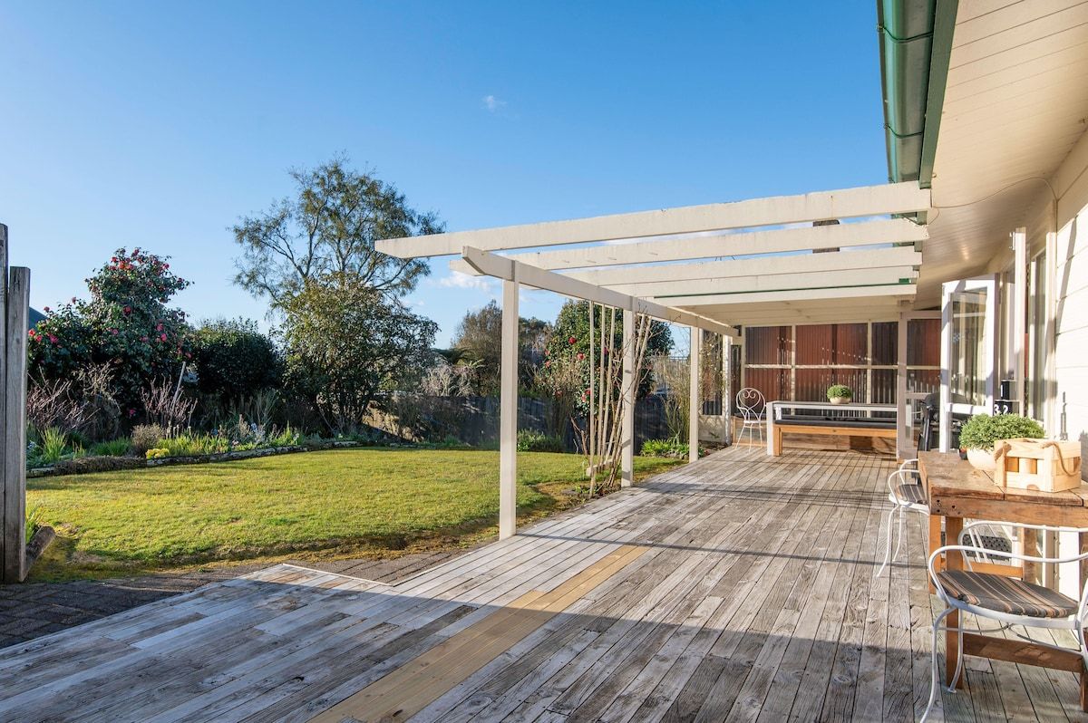 Una terraza de madera con una pérgola, un banco y una mesa con sillas.