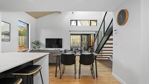 A modern kitchen with a dining area, wooden flooring, and a staircase leading to an upper level. - The Sanctuary - Modern, Spa Pool, Sleeps 4 (Rotorua)